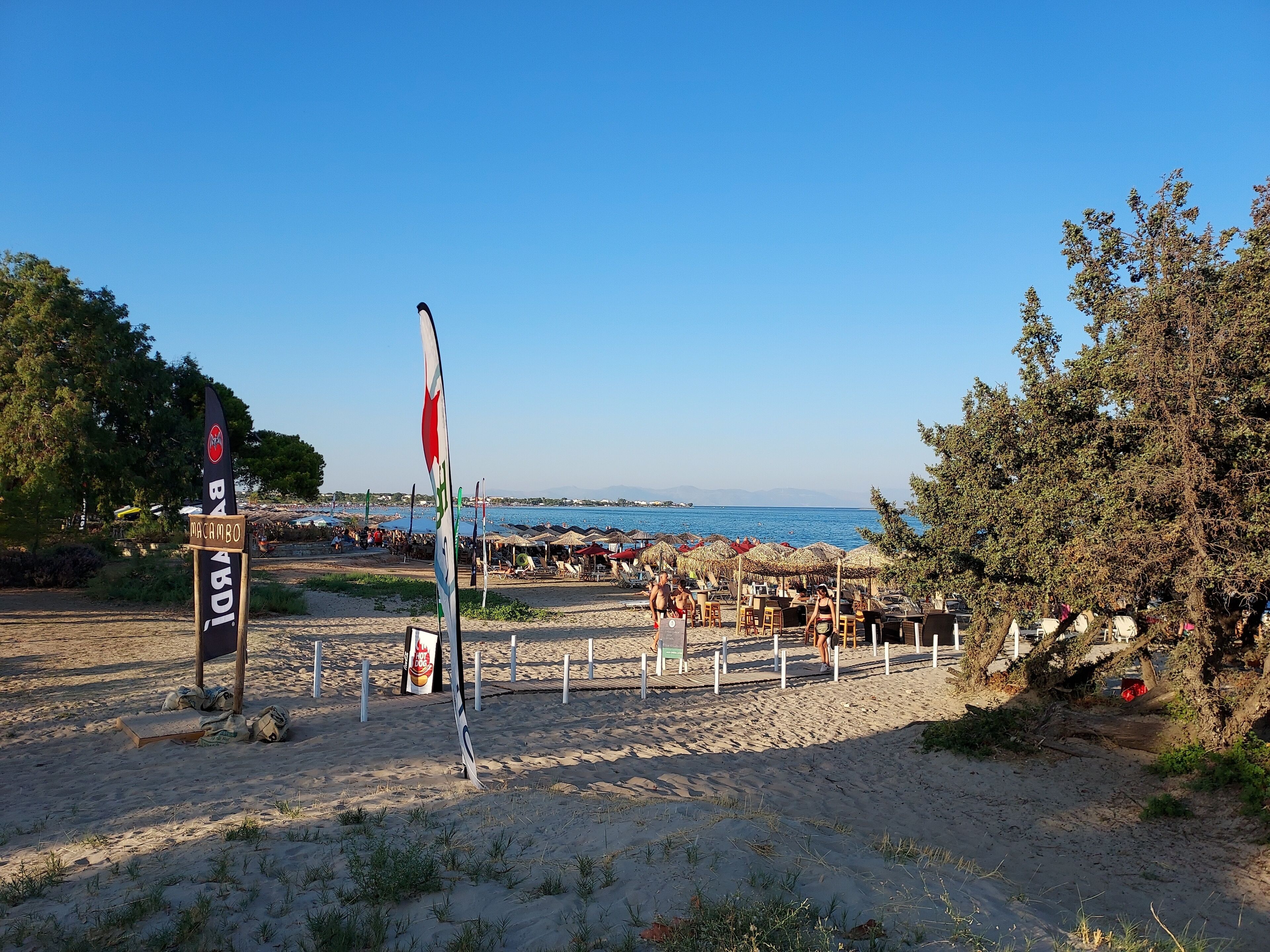 Una playa con una bandera, sombrillas y vista al mar.