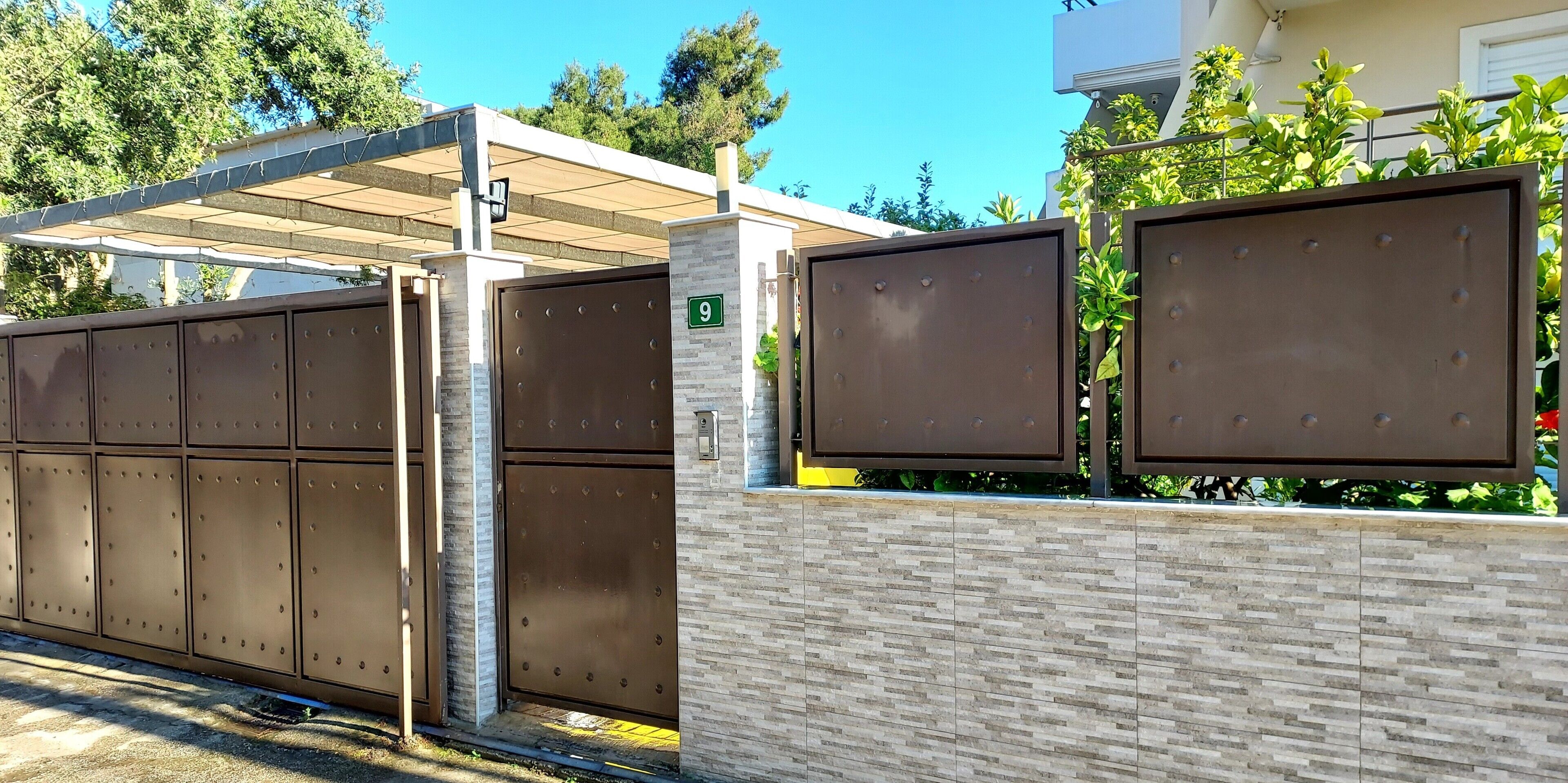 Ein verschlossenes Tor mit Metallgitter, einer Hausnummer und einem überdachten Parkbereich.