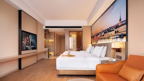 A hotel room with a bed, a sofa, a TV, and a painting of a cityscape. - Venus International Hotel  (Changsha)