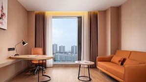 A modern hotel room with a view of high-rise buildings, a desk with a lamp, a sofa, and a small table. - Venus International Hotel  (Changsha)