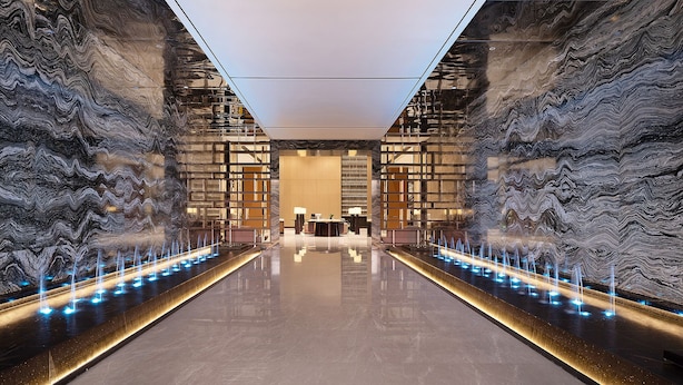A modern lobby with a reflective floor, a central reception desk, and a water feature with illuminated jets. - Venus International Hotel  (Changsha)