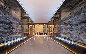A modern lobby with a reflective floor, a central reception desk, and a water feature with illuminated jets. - Venus International Hotel  (Changsha)
