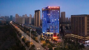 A modern hotel with a prominent glass facade, surrounded by high-rise buildings and a busy street at dusk. - Venus International Hotel  (Changsha)