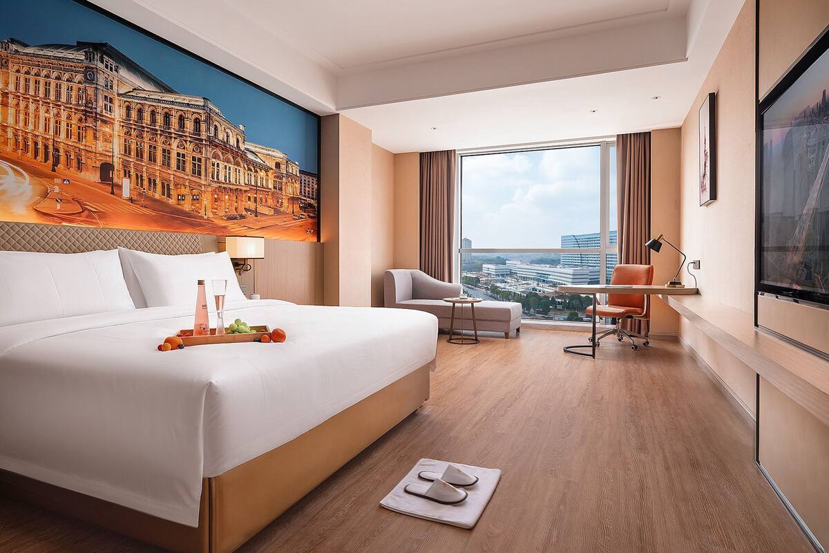 Habitación de hotel con una cama grande, escritorio, silla, televisor y vista panorámica de la ciudad.