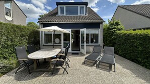 Ein Haus mit einer Terrassenfläche, ausgestattet mit einem Tisch, Stühlen und einem Sonnenschirm, mit Kiesboden.