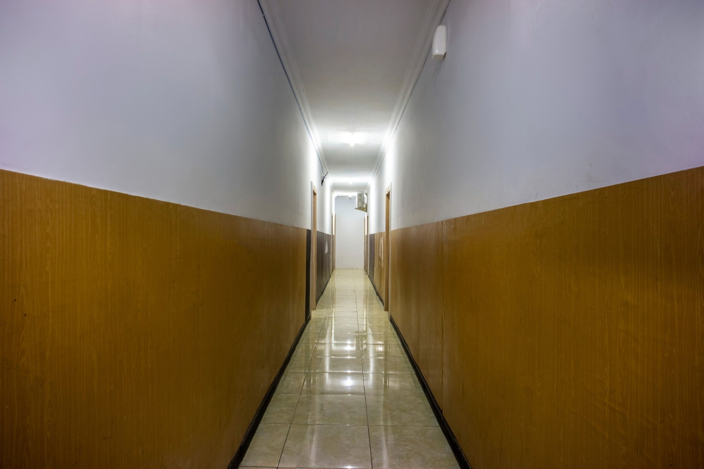 A long, narrow hallway with wooden paneling on the walls and a shiny tiled floor.