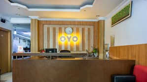 A reception desk with a wooden finish and a clock above it. - Hotel O Wisma Permata Makassar (Makassar)