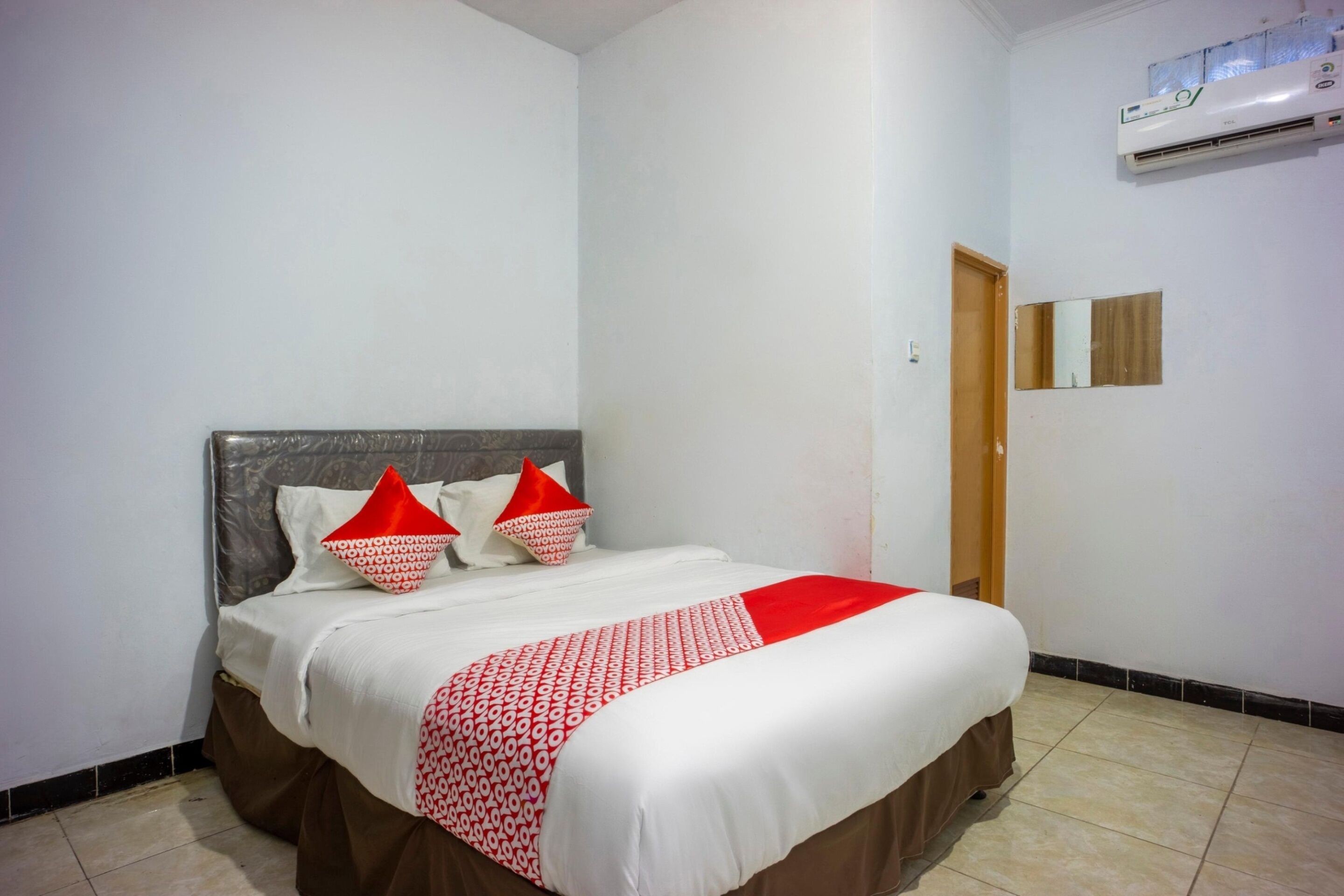 A neatly made bed with a white and red bedspread, two red pillows, and a brown skirted bed base.