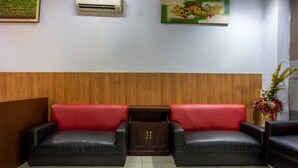 A reception area with two black leather sofas with red cushions, a wooden cabinet, an air conditioning unit, and a floral painting on the wall. - Hotel O Wisma Permata Makassar (Makassar)