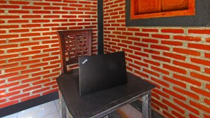 A laptop on a small table in a room with a brick wall and a wooden chair. - OYO 92308 Kos Duduk (Janapria)