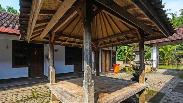 A wooden gazebo with a tiled roof, a stone bench, and a cobblestone pathway. - OYO 92308 Kos Duduk (Janapria)