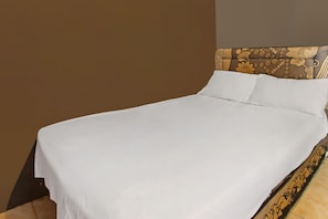 A neatly made bed with white linens and a headboard with a floral pattern.