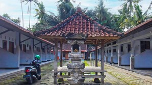 A traditional pavilion with a tiled roof, surrounded by a corridor with white walls and a cobblestone floor. - OYO 92308 Kos Duduk (Janapria)