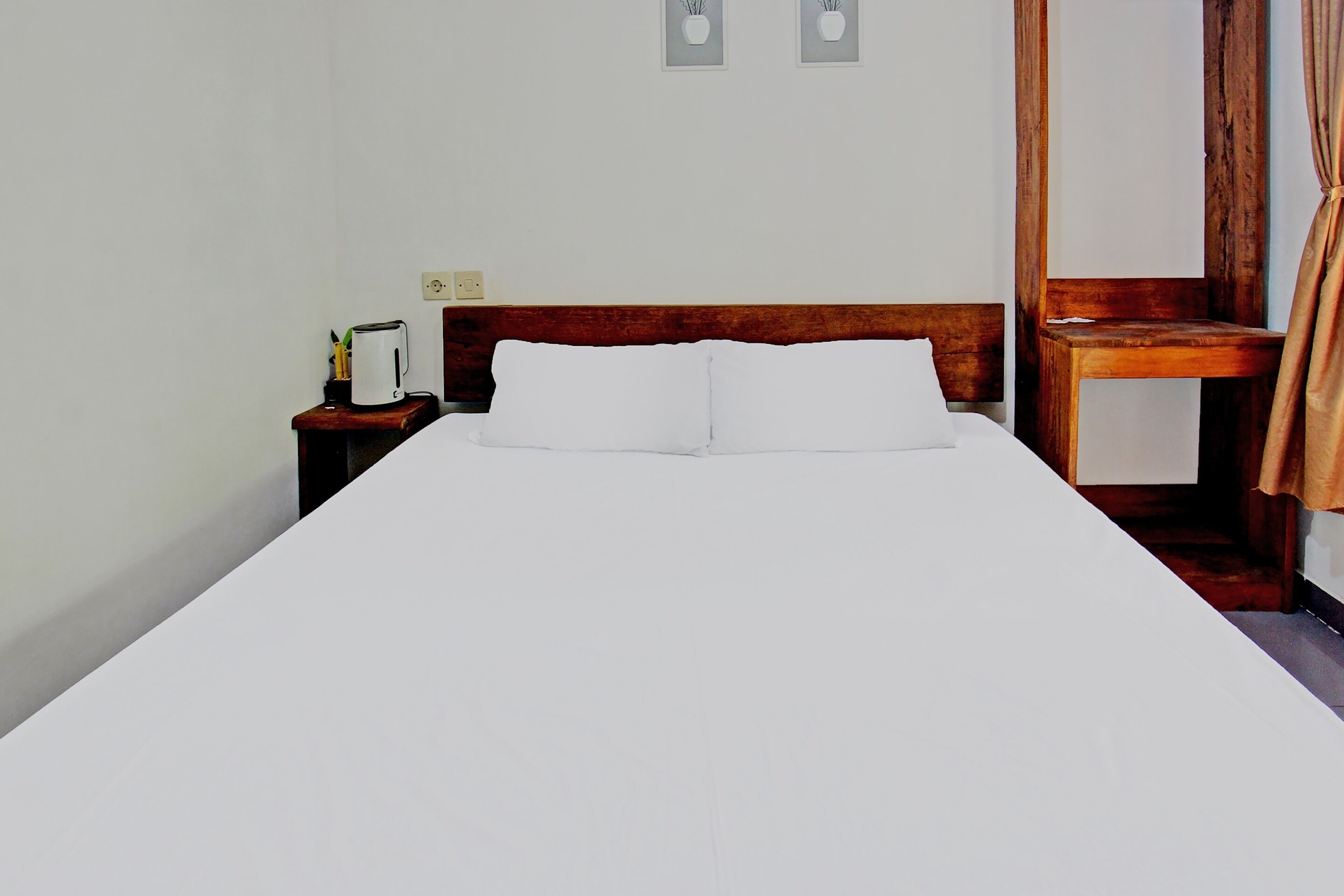 A neatly made bed with white linens in a simple room with a wooden headboard.