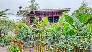 Ein rustikales Holzhaus mit großen Fenstern, umgeben von üppiger tropischer Vegetation.