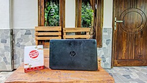 Ein Laptop steht auf einem Holztisch, neben ihm ein Schild.