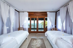 Une chambre avec deux lits, un plafond en bois et une vue sur la mer par une porte vitrée.