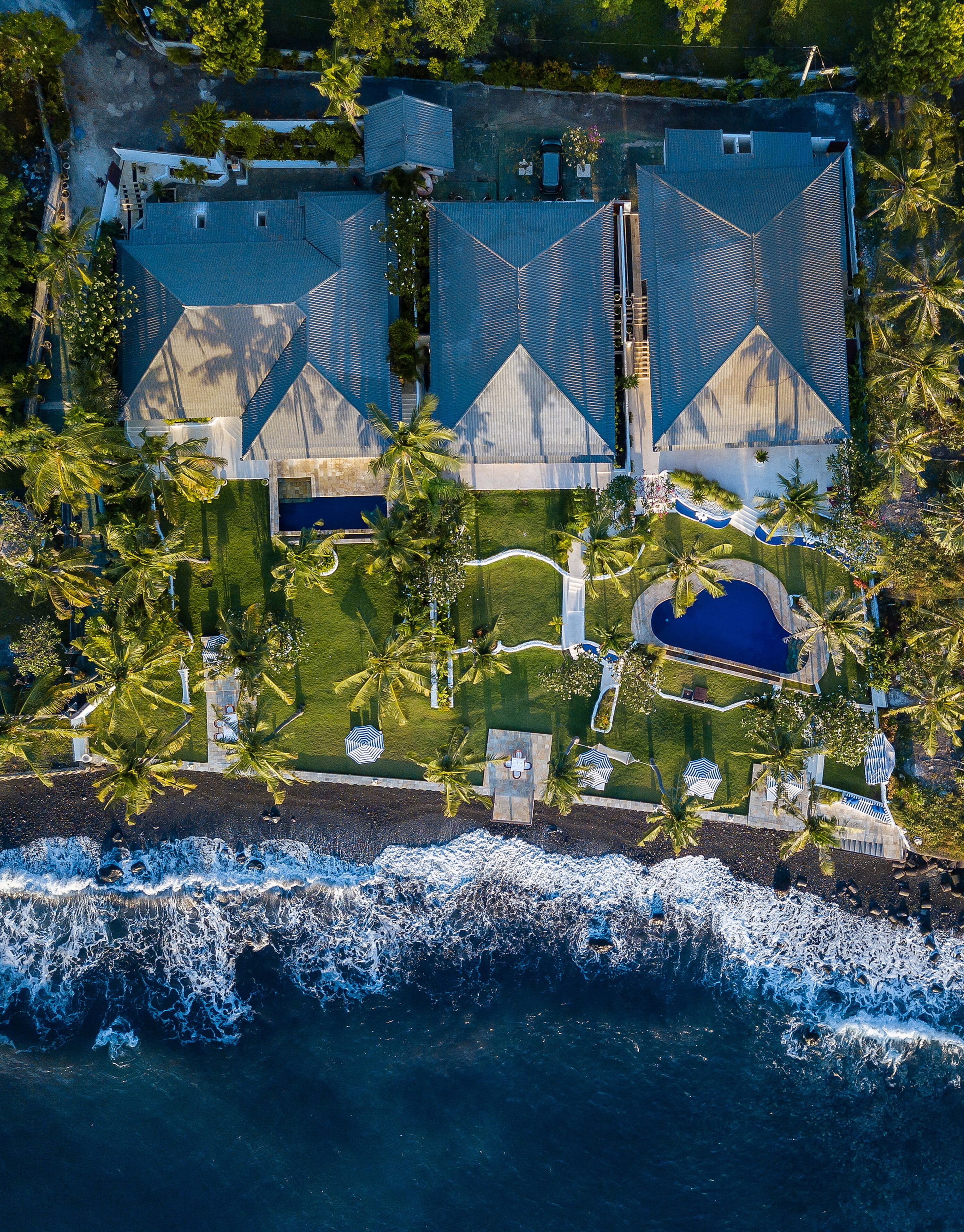 An aerial view of a coastal property with a large house, a swimming pool, and a beach area.