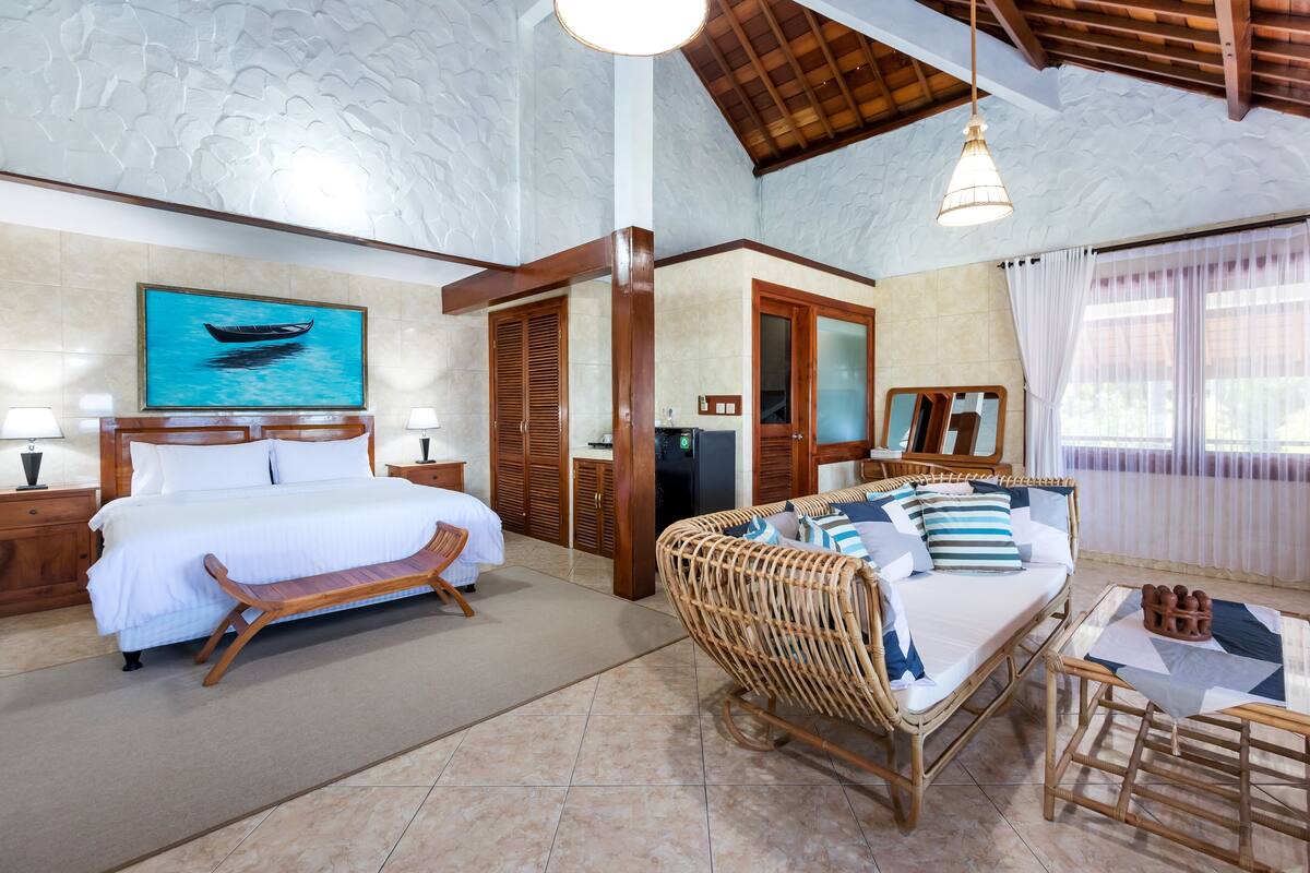 A spacious room with a large bed, a wicker sofa, a dining table, and a ceiling with a textured design.