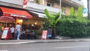 A restaurant with outdoor seating, a red awning, and a sign advertising Swiss food.
