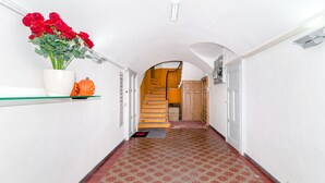 A hallway with a tiled floor, a white wall, a shelf with a vase of flowers, and a staircase leading to an upper level.