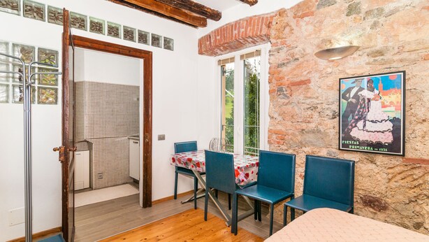 A room with a wooden floor, a dining table with chairs, a window with a view, and a poster on the wall.