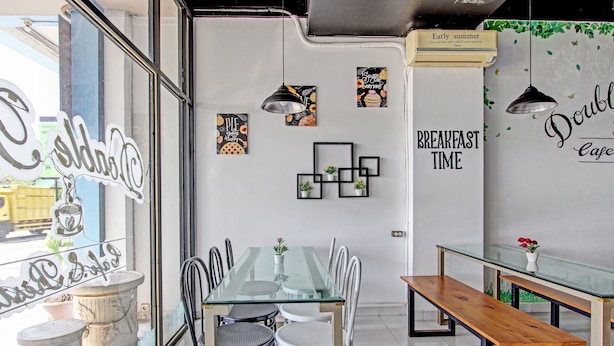 A modern cafe interior with a glass dining table, white chairs, and a wooden bench. - Capital O 92295 Double Tree (Purwokerto)