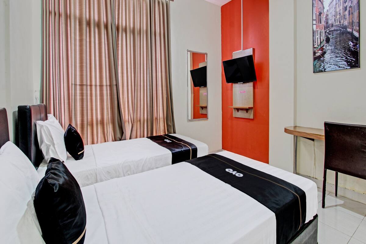 A hotel room with two beds, a desk, a chair, a TV, and a window with curtains.