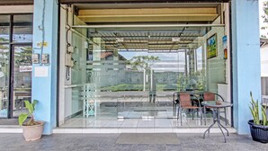 A glass-fronted entrance with a covered patio area, outdoor seating, and a potted plant. - Capital O 92295 Double Tree (Purwokerto)