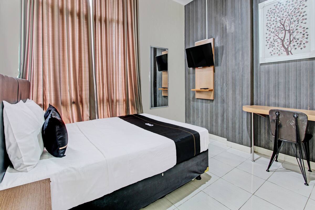A hotel room with a bed, a desk, a chair, a TV, and a painting on the wall.