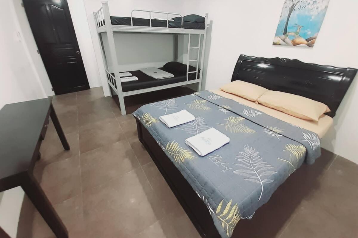Une chambre avec un lit superposé, un lit simple, un bureau et un tableau accroché au mur.