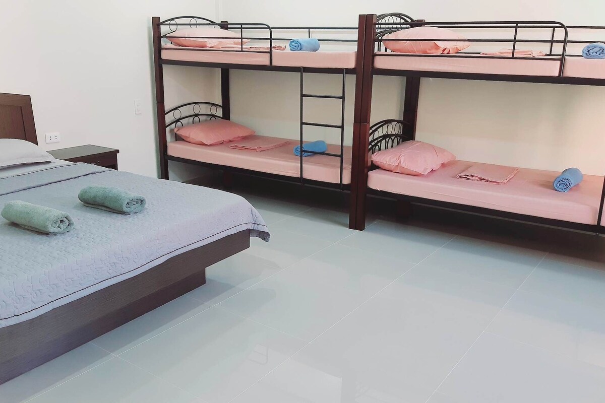 Cama litera con dos niveles, cada uno con colchón y almohadas. A la izquierda, una cama individual con colchón y almohadas.