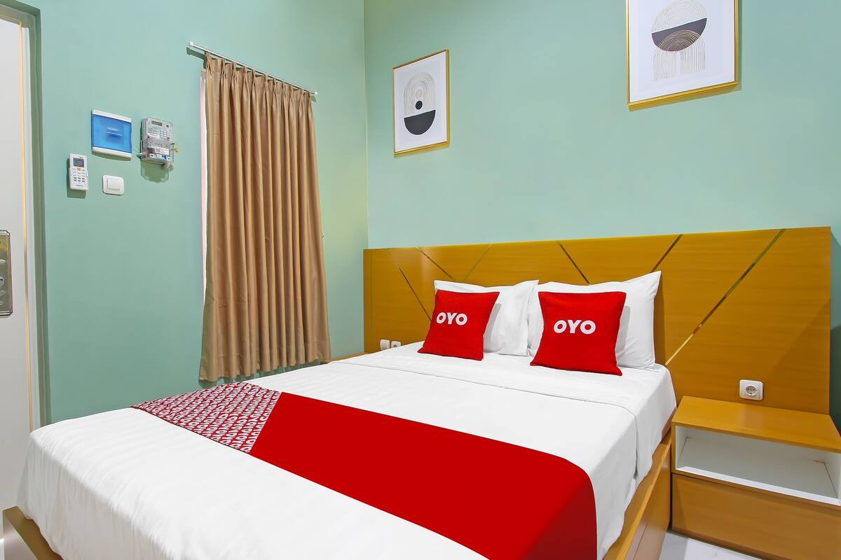 Quarto de hotel com cama, mesa de cabeceira, telefone na parede e cortina.