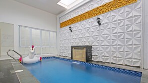 An indoor swimming pool with a white geometric wall design, a decorative golden border, and a black fireplace. - Capital O 92105 A'shanti Inn (Cilacap)