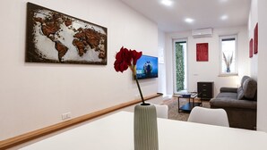 Un salón moderno con una mesa blanca, una gran obra de arte con un mapa del mundo, un jarrón rojo, un sofá gris y un televisor.