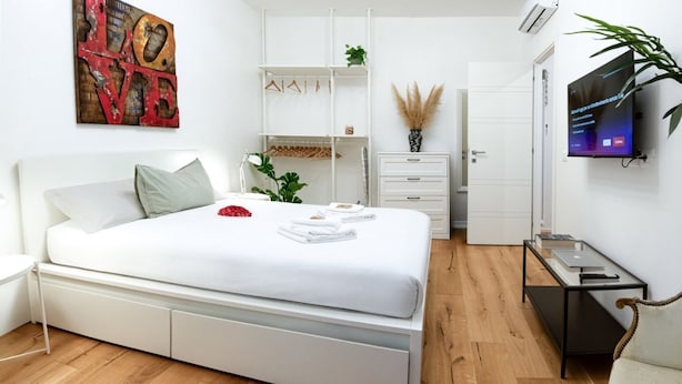 Un dormitorio moderno con una cama blanca, un televisor y un armario.