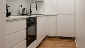 Una cocina compacta con muebles blancos, un grifo negro, una tetera y un horno empotrado.