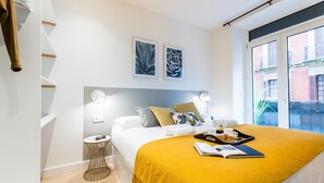A modern bedroom with a bed, bedside table, and a window with a view of buildings.