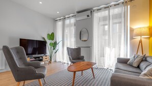 A modern living room with a grey sofa, a grey armchair, a wooden coffee table, a TV, and a potted plant.