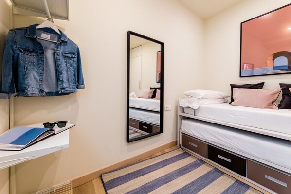 A bedroom with a bunk bed, a hanging denim jacket, a mirror, and a framed picture on the wall.