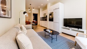 Ein modernes Wohnzimmer mit einer Couch, einem Couchtisch, einem Fernseher und einer Küchenzeile im Hintergrund.