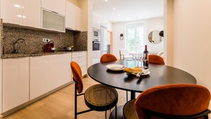 Eine moderne Küche mit weißen Schränken, Granit Arbeitsplatten und einem Essbereich mit rundem Tisch und orangefarbenen Stühlen.