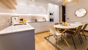 A modern kitchen with white cabinetry, a built-in oven, and a dining area with a round table and chairs.