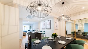 A modern dining area with a long table set for six, green chairs, and pendant lights. - GRAN VIA SUITE: superior apartment for 6 PAX. 2min from the beach (San Sebastián)