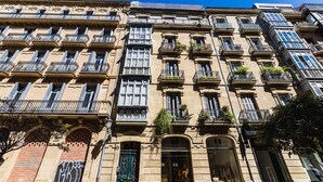 A multi-story building with a classic architectural style, featuring balconies with plants, large windows, and a prominent entrance with a green door. - GETARIA SUITE: superior apartment for 4 PAX. Pedestrian street. 2min walk from La Concha beach (San Sebastián)