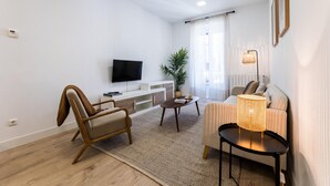 A modern living room with a flat-screen TV, a sofa, a chair, a coffee table, and a floor lamp. - GETARIA SUITE: superior apartment for 4 PAX. Pedestrian street. 2min walk from La Concha beach (San Sebastián)