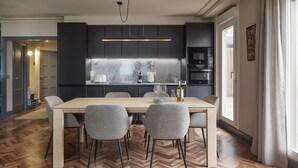 Una cocina moderna con armarios oscuros, un salpicadero de mármol y una zona de comedor con mesa de madera y sillas grises.