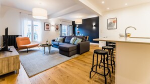 A modern living room with a sofa, ottoman, and a coffee table. There is a kitchen area with a bar stool and a dining table. - ZABALETA SUITE: 6 PAX Superior apartment. Practical and distinguished. 500 meters from the beach (San Sebastián)