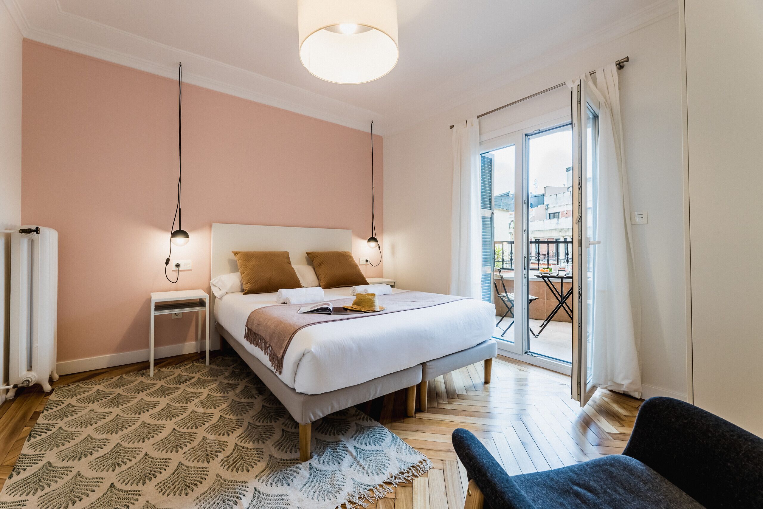 A bedroom with a bed, bedside tables, a patterned rug, and a view through a sliding glass door to an outdoor area.