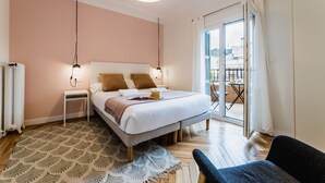 A bedroom with a bed, bedside tables, a patterned rug, and a view through a sliding glass door to an outdoor area. - ZABALETA SUITE: 6 PAX Superior apartment. Practical and distinguished. 500 meters from the beach (San Sebastián)